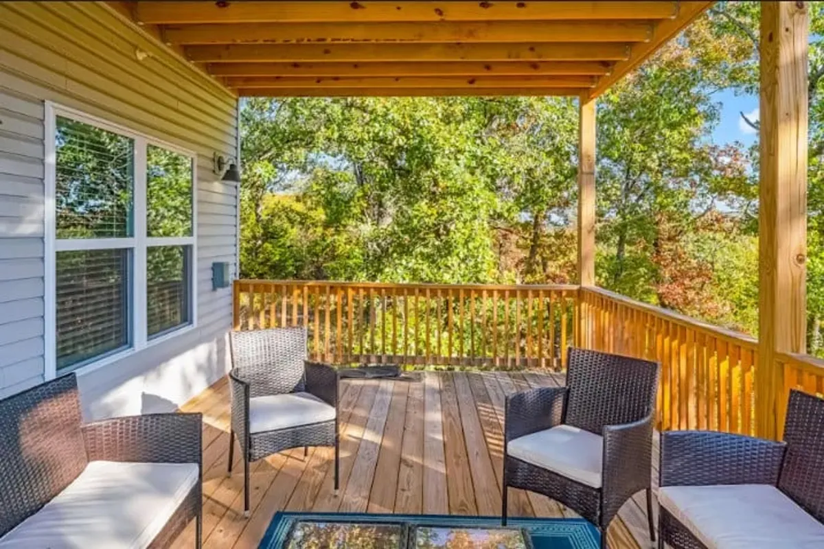 A peaceful wooden deck furnished with wicker chairs and a glass coffee table, surrounded by lush greenery. The mood is tranquil, with hints of laughter and conversation, making it a perfect setting for both quiet moments and socializing after indoor activities.