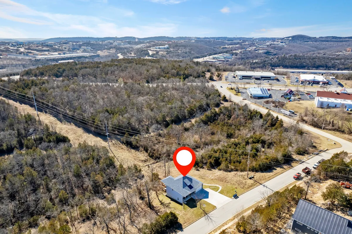 A broad exterior view of the house surrounded by greenery and a peaceful roadway, highlighting the property's integration with the natural Ozark setting. The image conveys the sense of retreat and the rural tranquility that defines the experience.