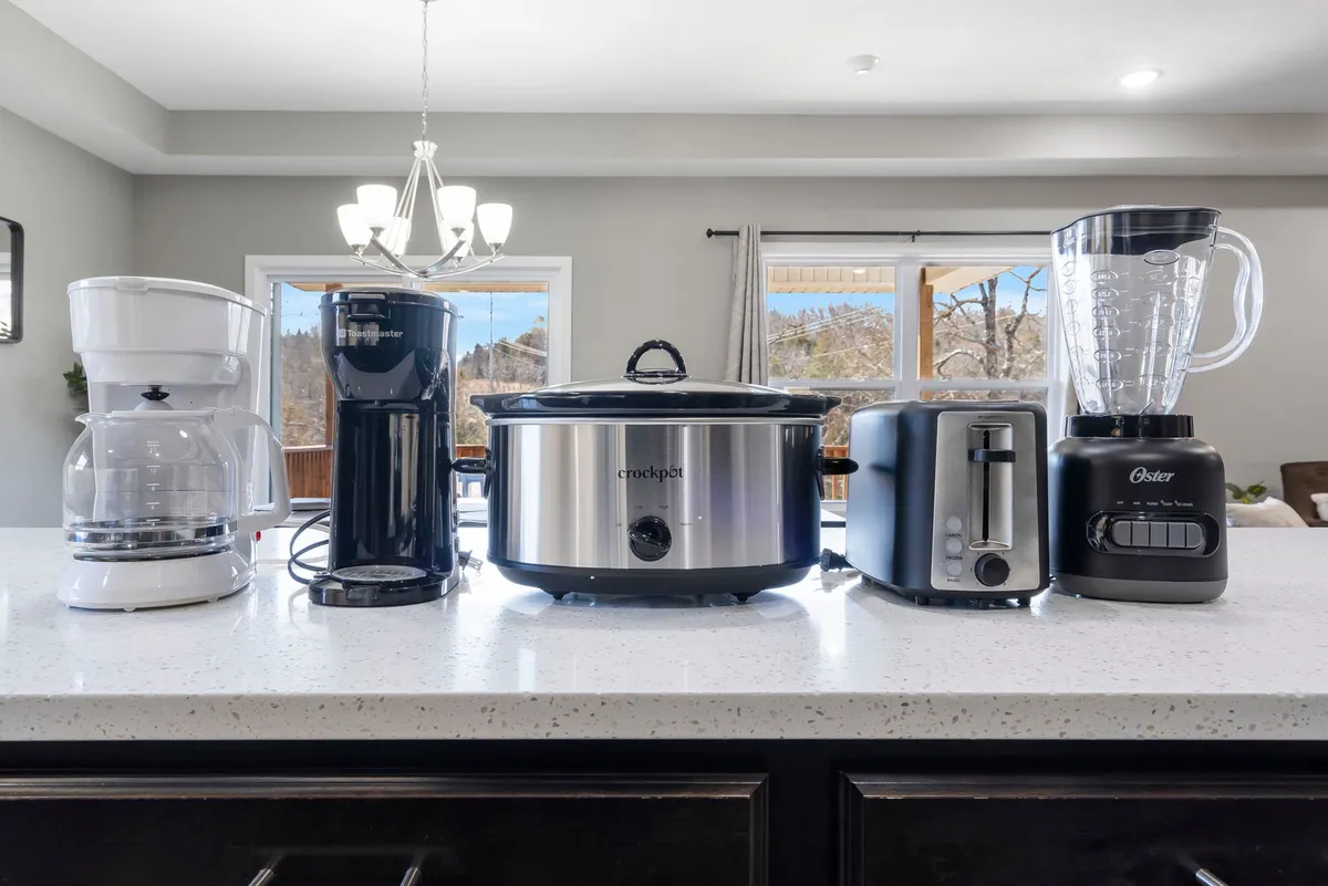 A close-up of the fully stocked kitchen, featuring modern appliances including a coffee maker, espresso machine, crockpot, toaster, and blender. The setup hints at delicious meals and morning rituals shared with family and friends.