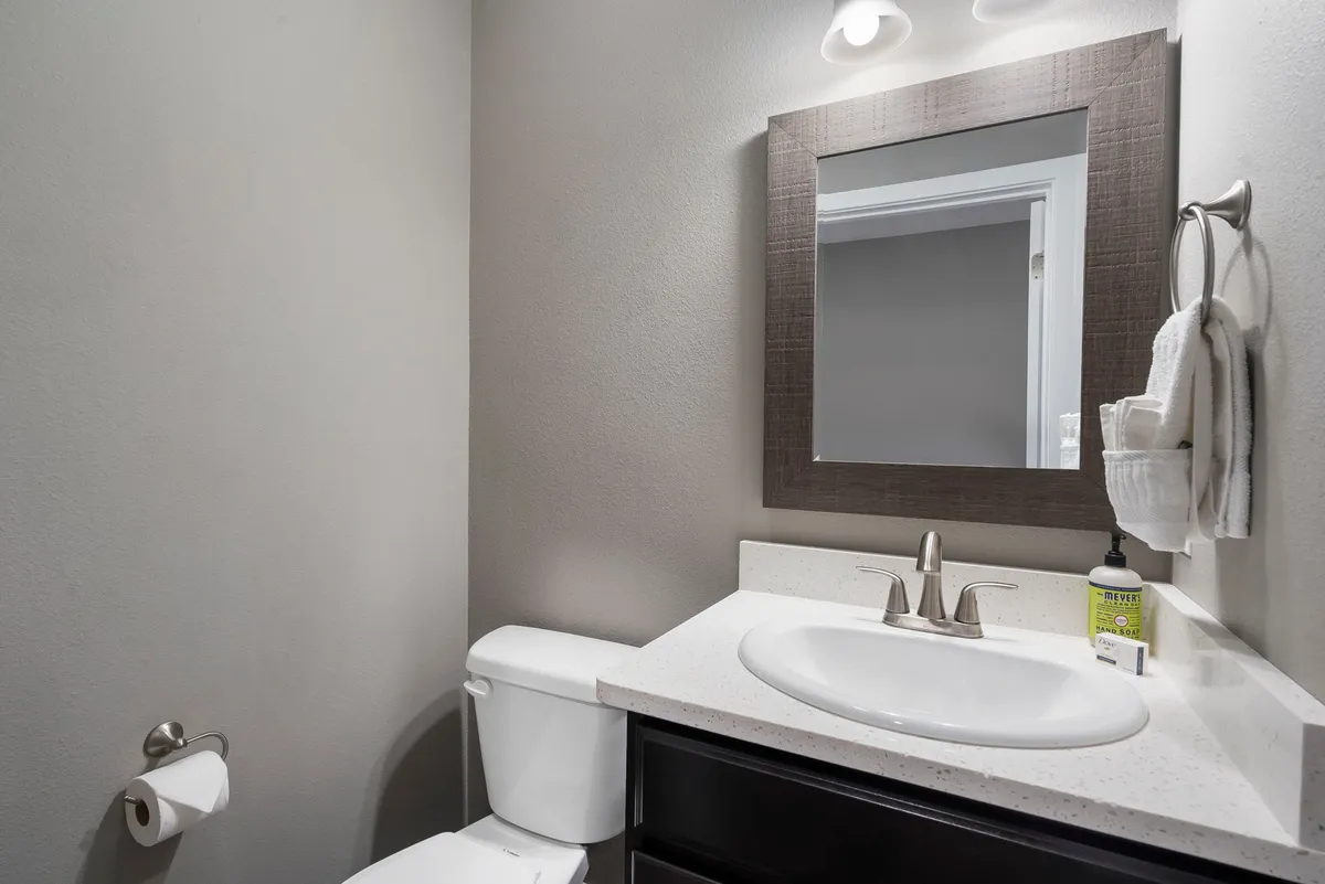 A functional and well-lit half bath, featuring a sink, mirror, and toilet. The compact design offers convenience for quick refreshment and supports hassle-free mornings for larger groups.