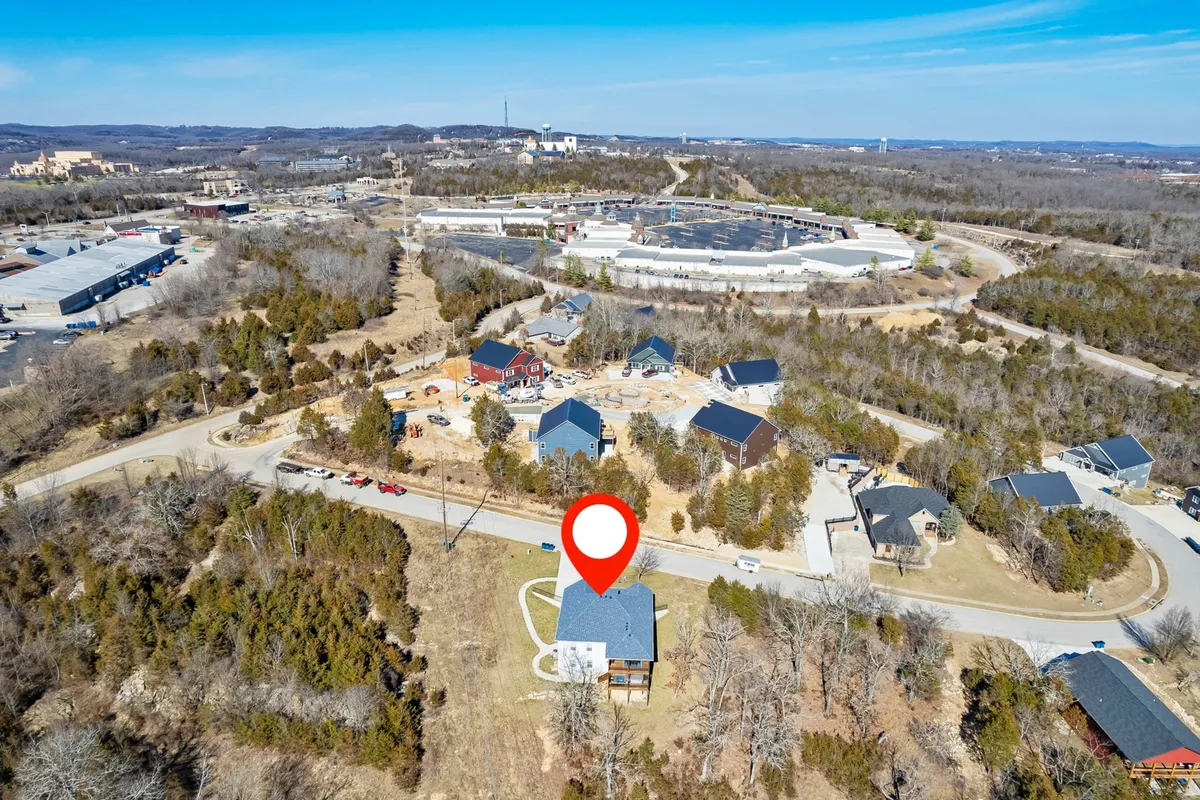 An exterior view featuring the house nestled among green trees, with nearby roads and buildings visible, evoking the idea of a well-placed base for exploration. The scene blends a sense of community and outdoor recreation, reinforcing the easy access to local events and attractions.